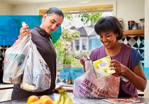 Ocado delivery driver handing grocery bags to a customer in her kitchen
